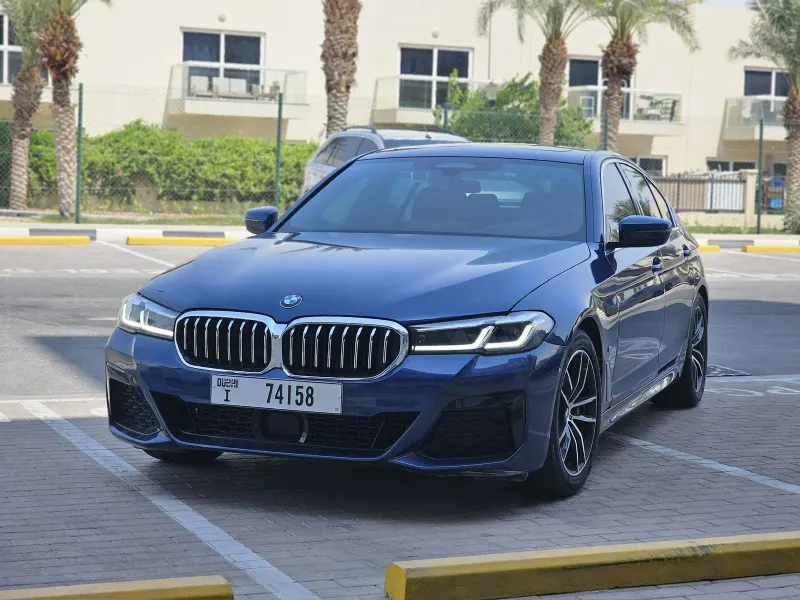 Blue BMW 520i 2023 sedan with Dubai plates in a residential car park, listed by Alrafaheia Car Rental