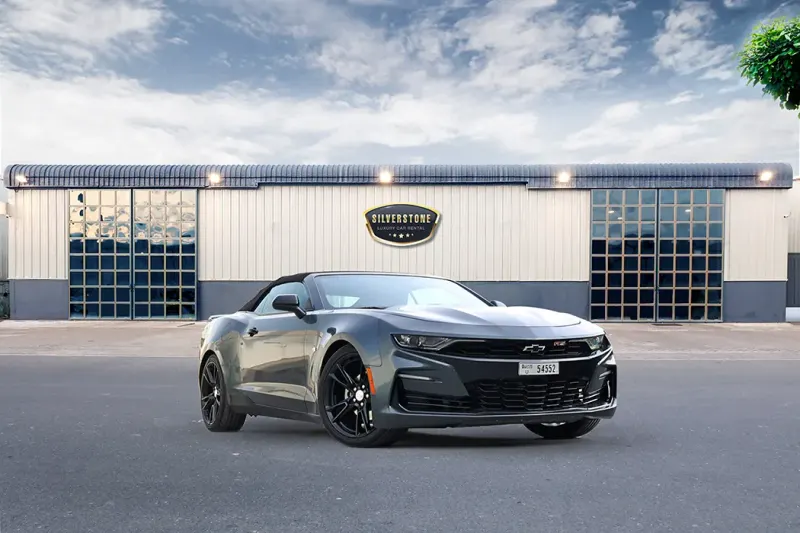 Grey Chevrolet Camaro Convertible 2021 with its black soft top up, parked in front of a Silverstone Car Rental building